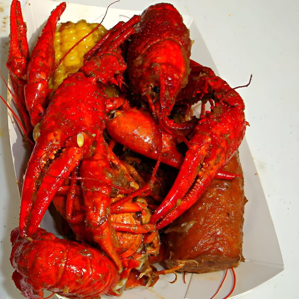 Boiled red crawfish, corn, and sausage in a white paper tray, a classic Cajun dish.