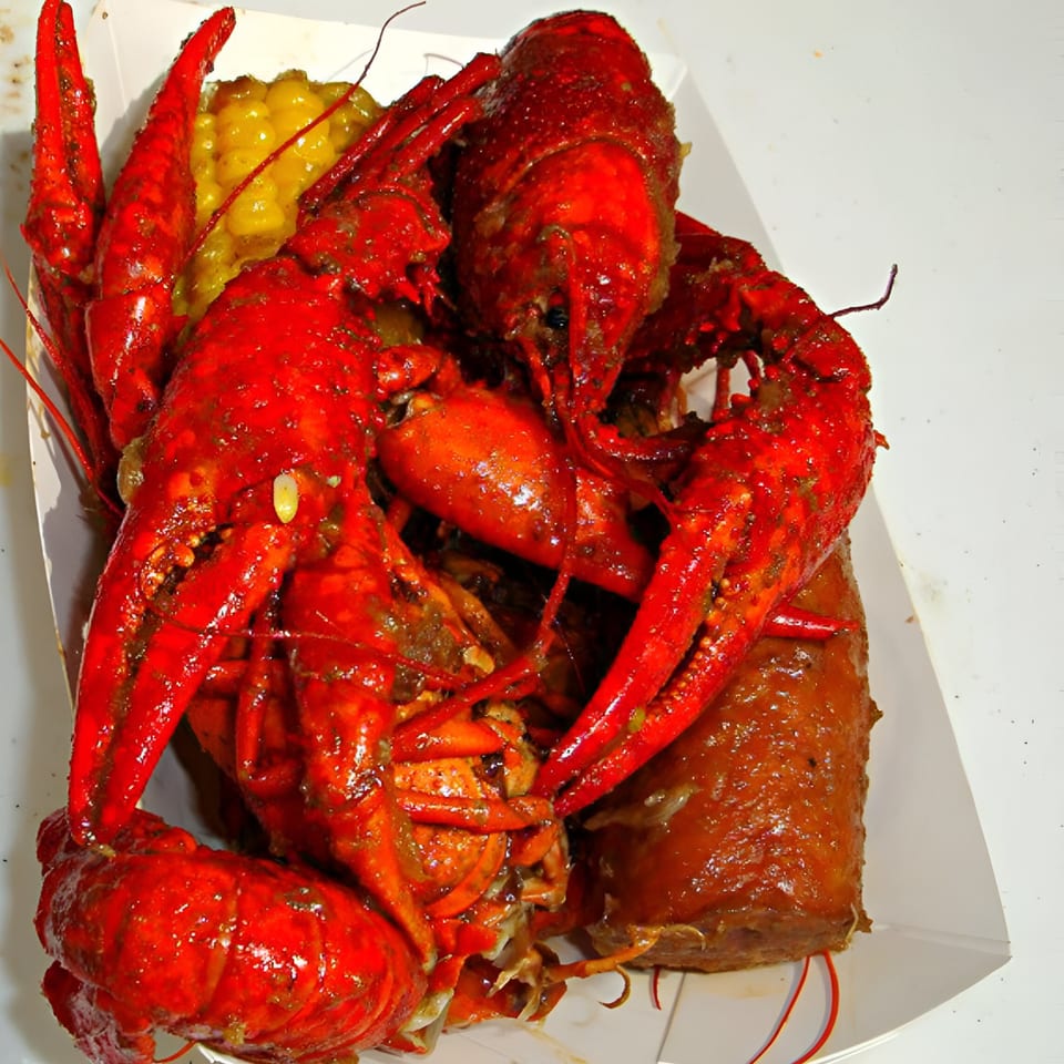 Boiled red crawfish, corn, and sausage in a white paper tray, a classic Cajun dish.