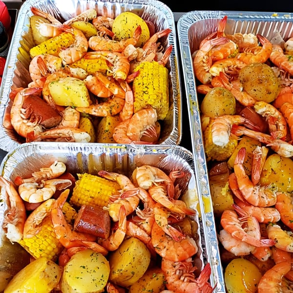 Three foil pans overflowing with Cajun shrimp, corn on the cob, potatoes, and sausage.
