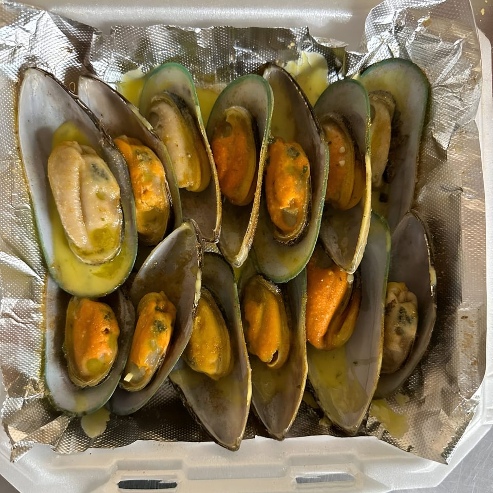 A Taste of New Orleans' Cajun mussels in a takeout container, with rich yellow sauce and foil lining.