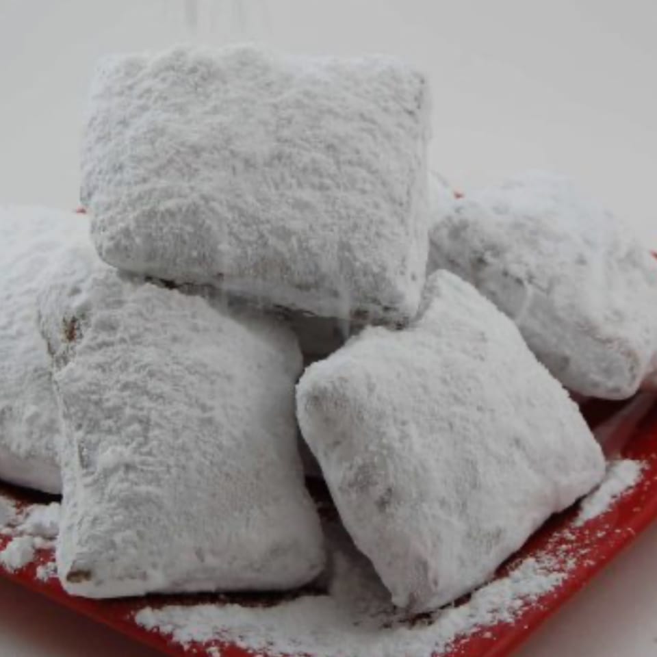 A pile of fluffy, square beignets generously dusted with powdered sugar on a red plate.