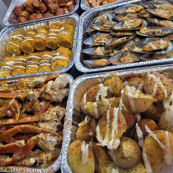 Cajun seafood boil with crab legs, mussels, corn, potatoes, and sausage in foil trays.