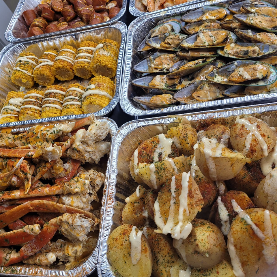 Cajun seafood boil with crab legs, mussels, corn, potatoes, and sausage in foil trays.