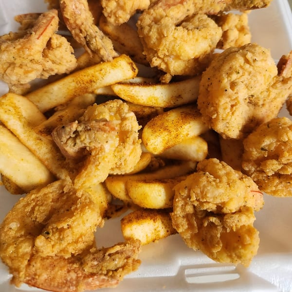 Close-up of golden-brown fried shrimp and seasoned french fries in a white container.