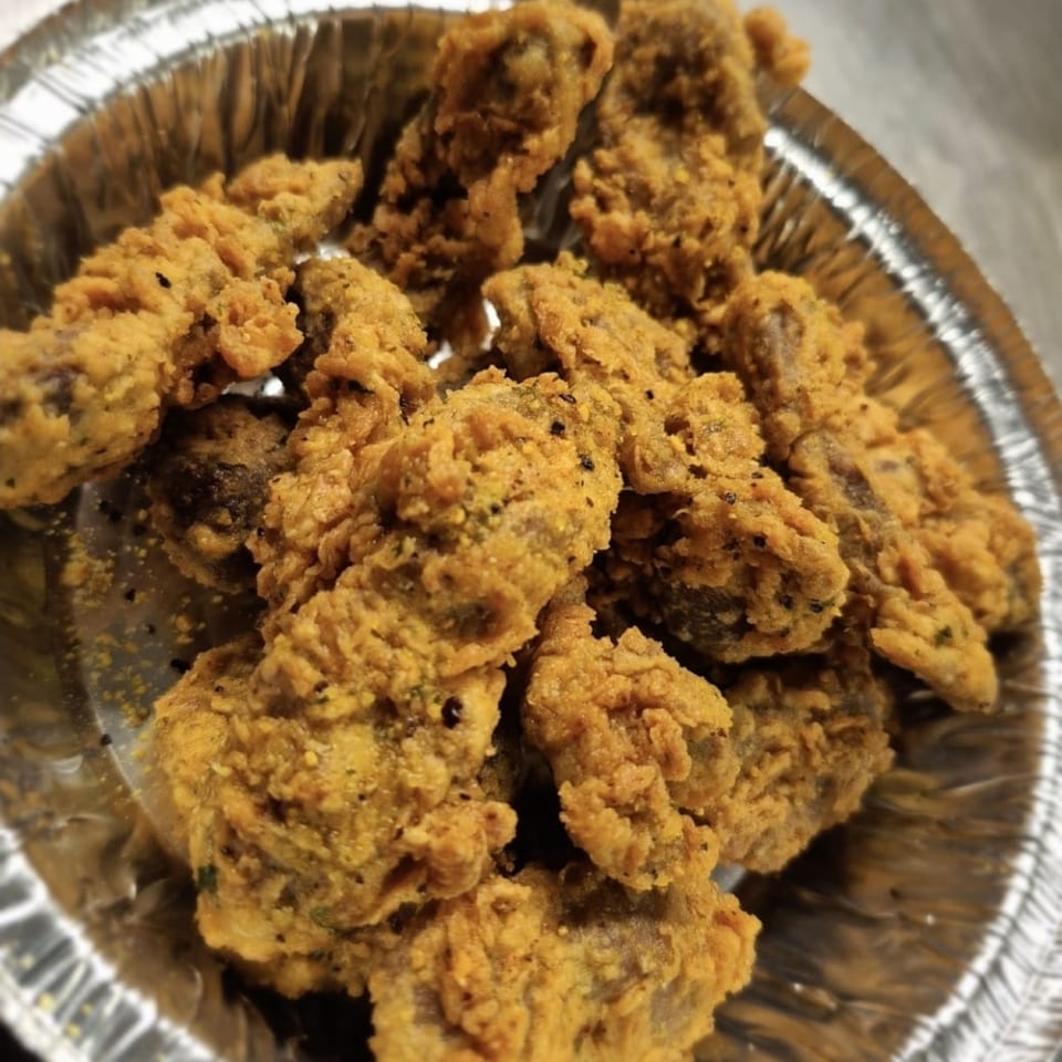 Close-up of golden-brown fried oysters, a Cajun specialty, in a silver foil container.