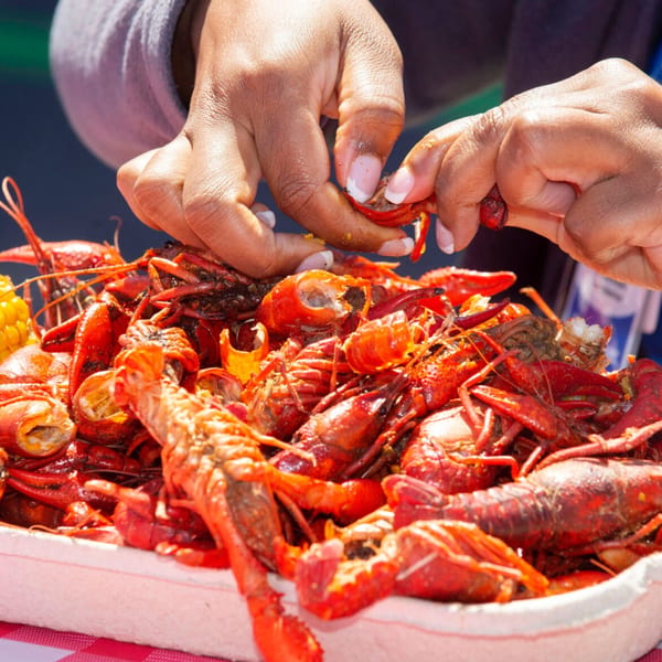Hands peeling a bright red crawfish from a large platter of Cajun crawfish boil.