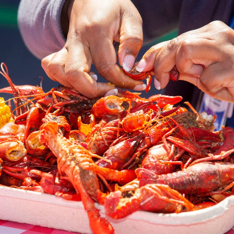 Hands peeling a bright red crawfish from a large platter of Cajun crawfish boil.