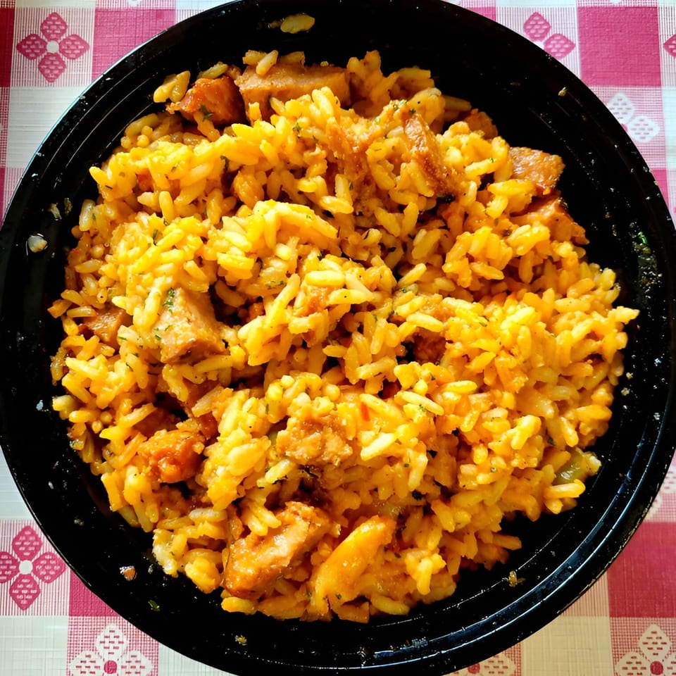 A close-up of Cajun jambalaya with rice and chicken in a black bowl on a checkered tablecloth.