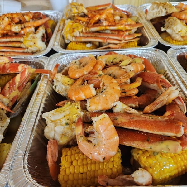 Several foil trays filled with Cajun-style shrimp, crab legs, and corn on the cob.
