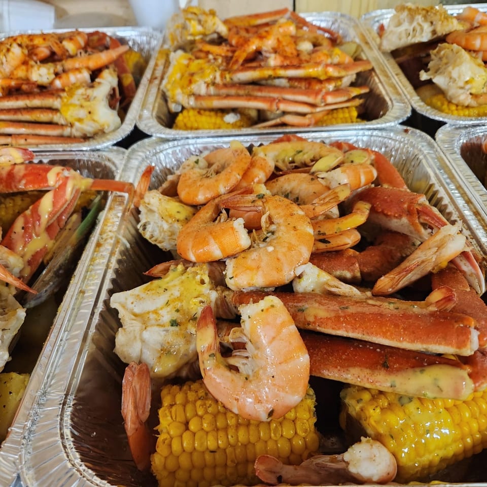Several foil trays filled with Cajun-style shrimp, crab legs, and corn on the cob.