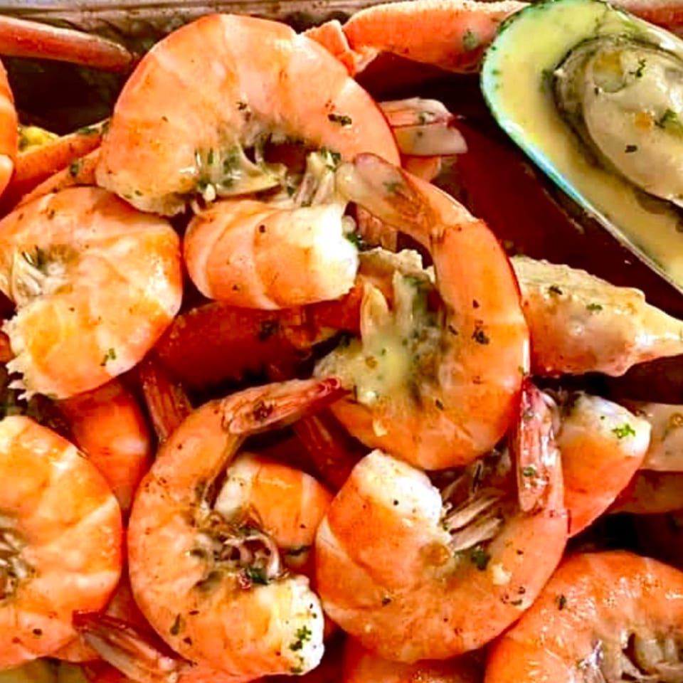 Close-up of Cajun-style shrimp and a green mussel, seasoned with herbs and spices.