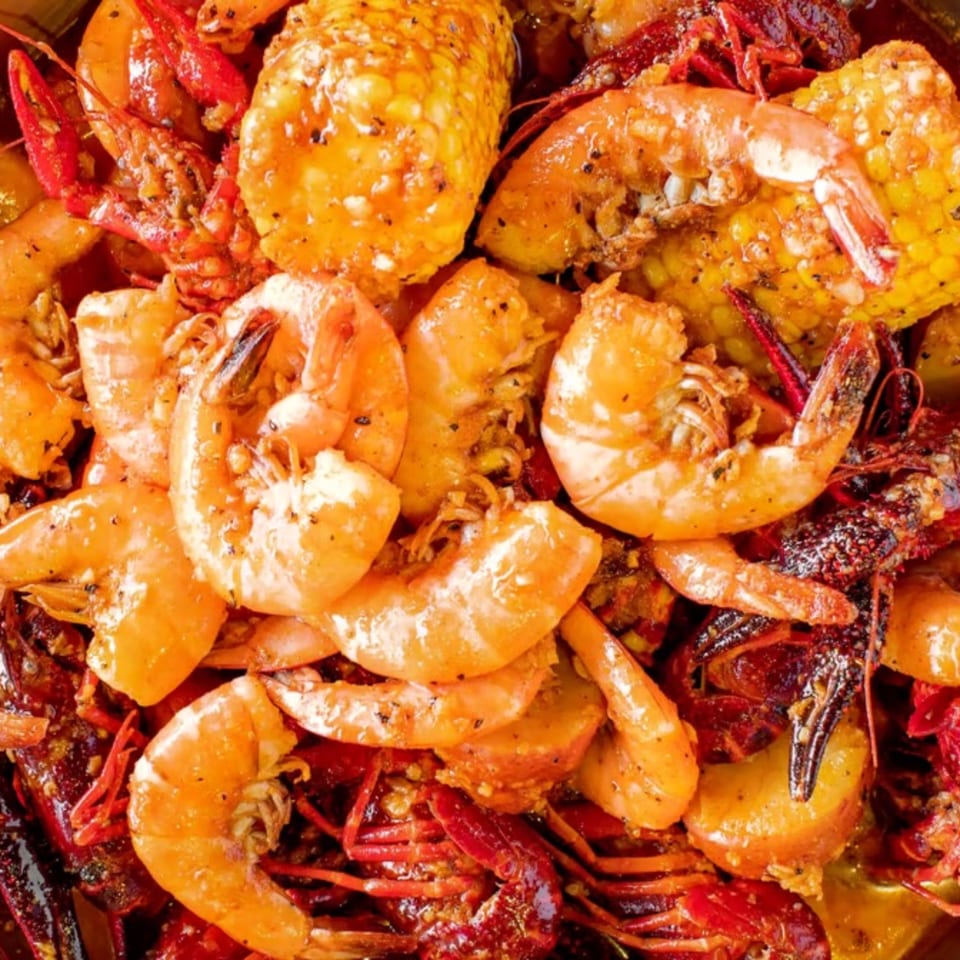 Close-up of a Cajun seafood boil with shrimp, crawfish, corn on the cob, and potatoes.