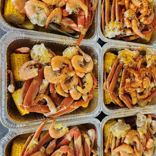 Multiple foil containers filled with Cajun shrimp, crab legs, and corn on the cob.